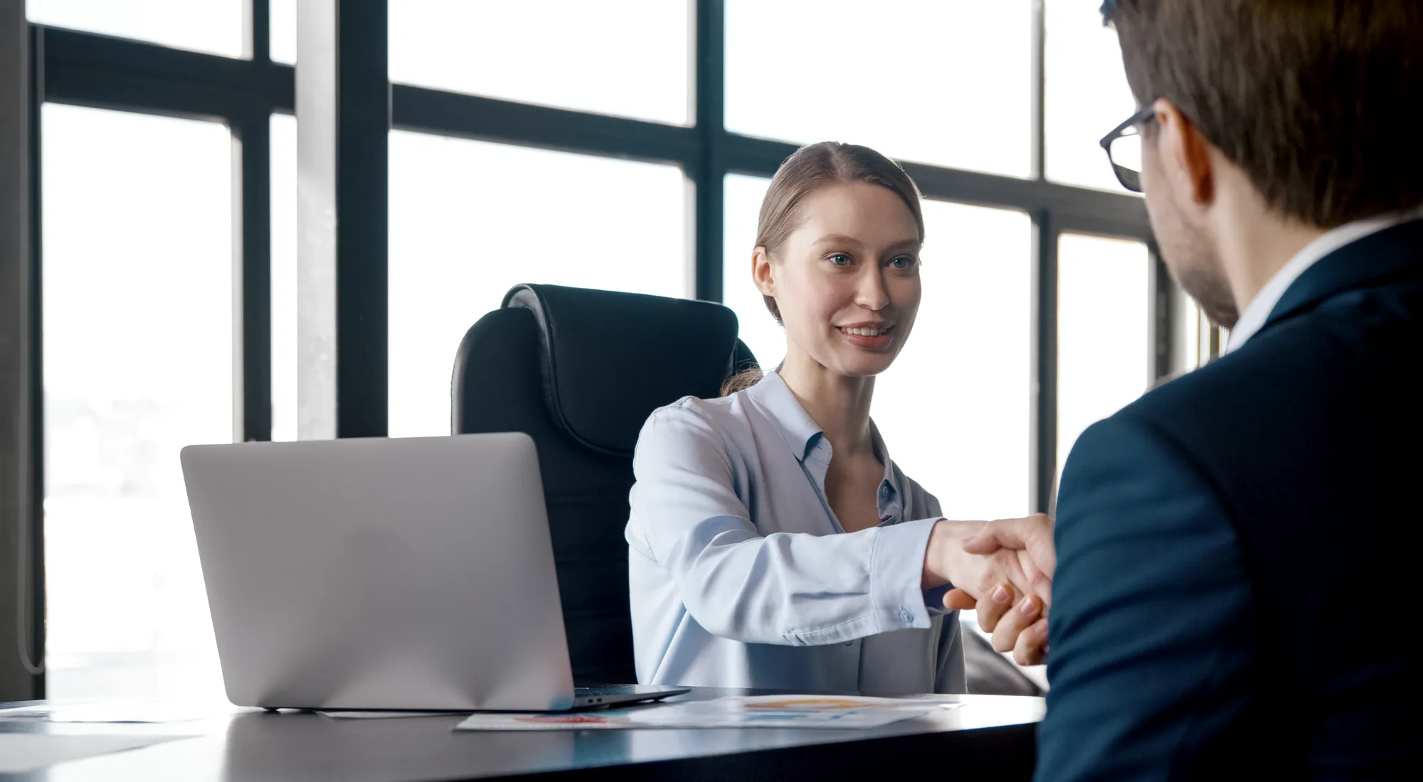 A recruiter and a candidate shaking hands across a desk